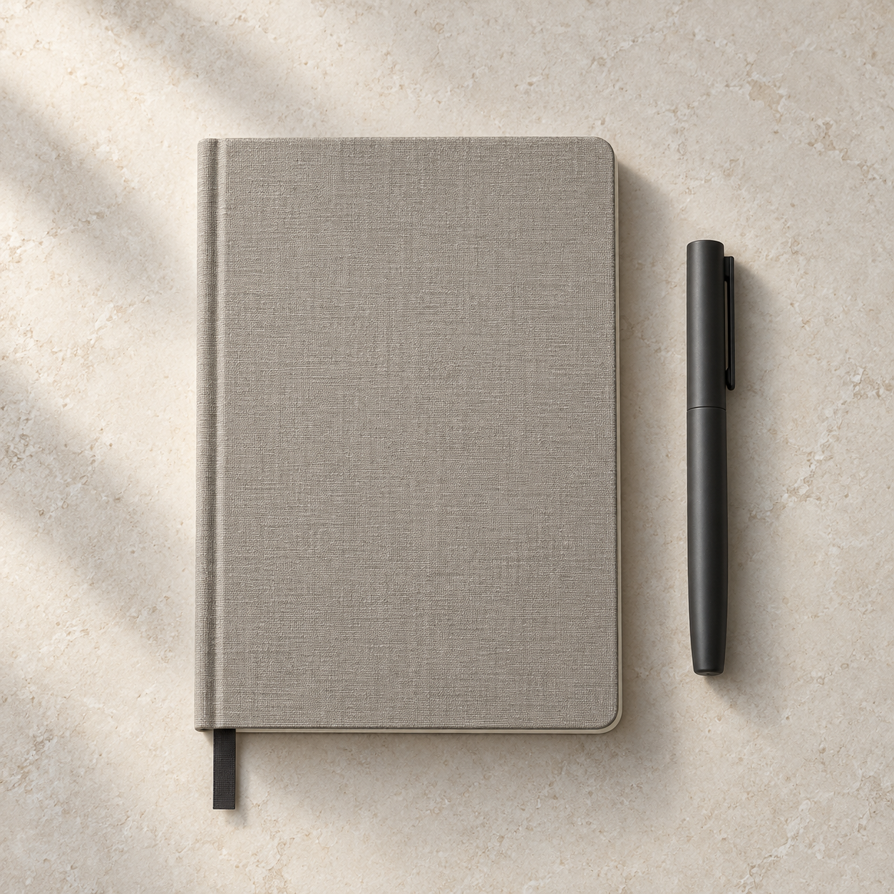 Warm gray linen notebook and matte charcoal pen on a stone desktop